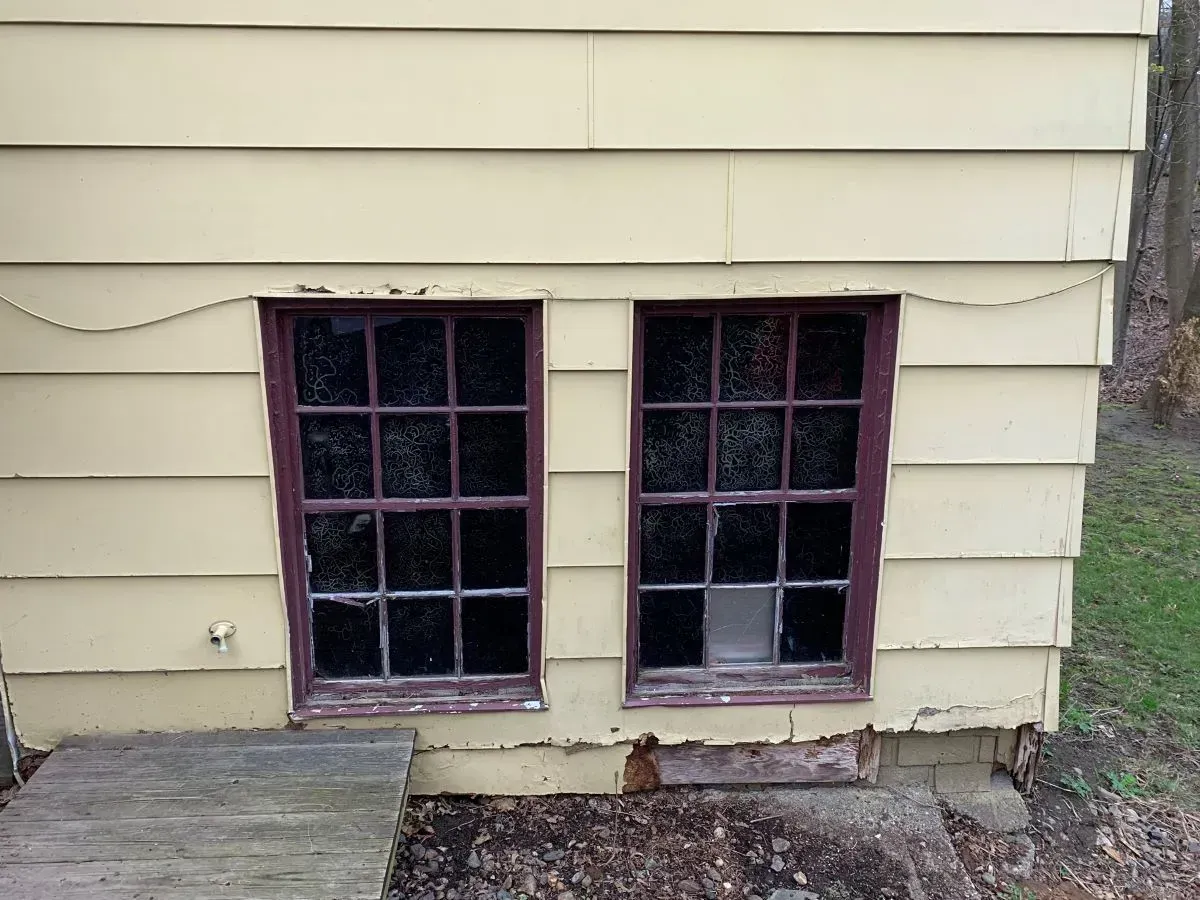Two windows on the side of a yellow house