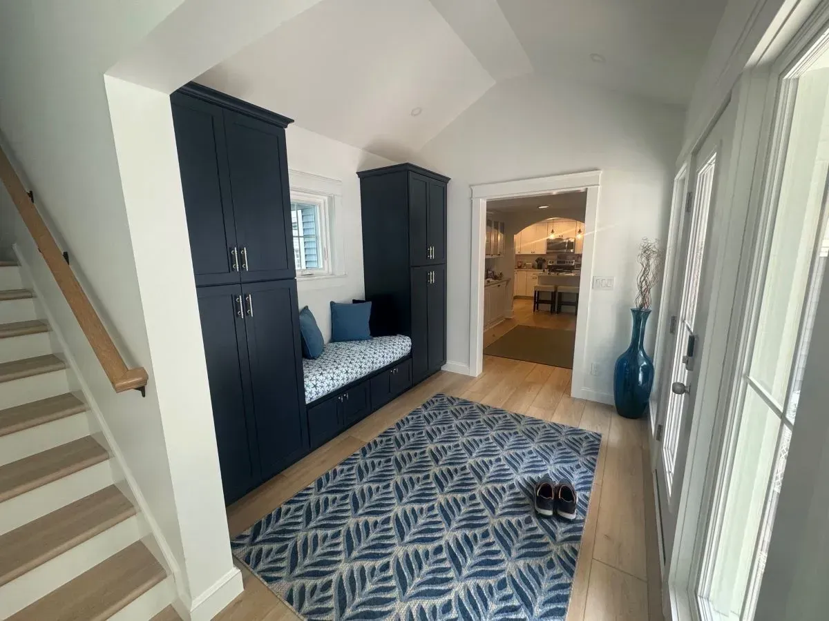 A hallway with stairs , a rug , and a bench.