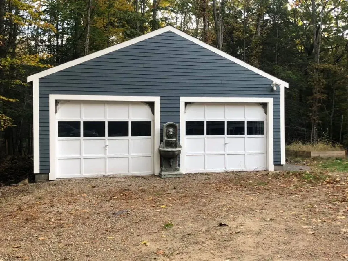 A garage with two garage doors is sitting in the middle of a dirt field.