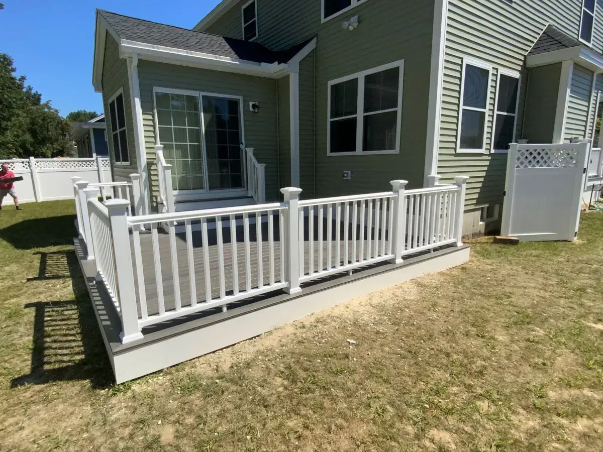 A green house with a white deck and fence in front of it.
