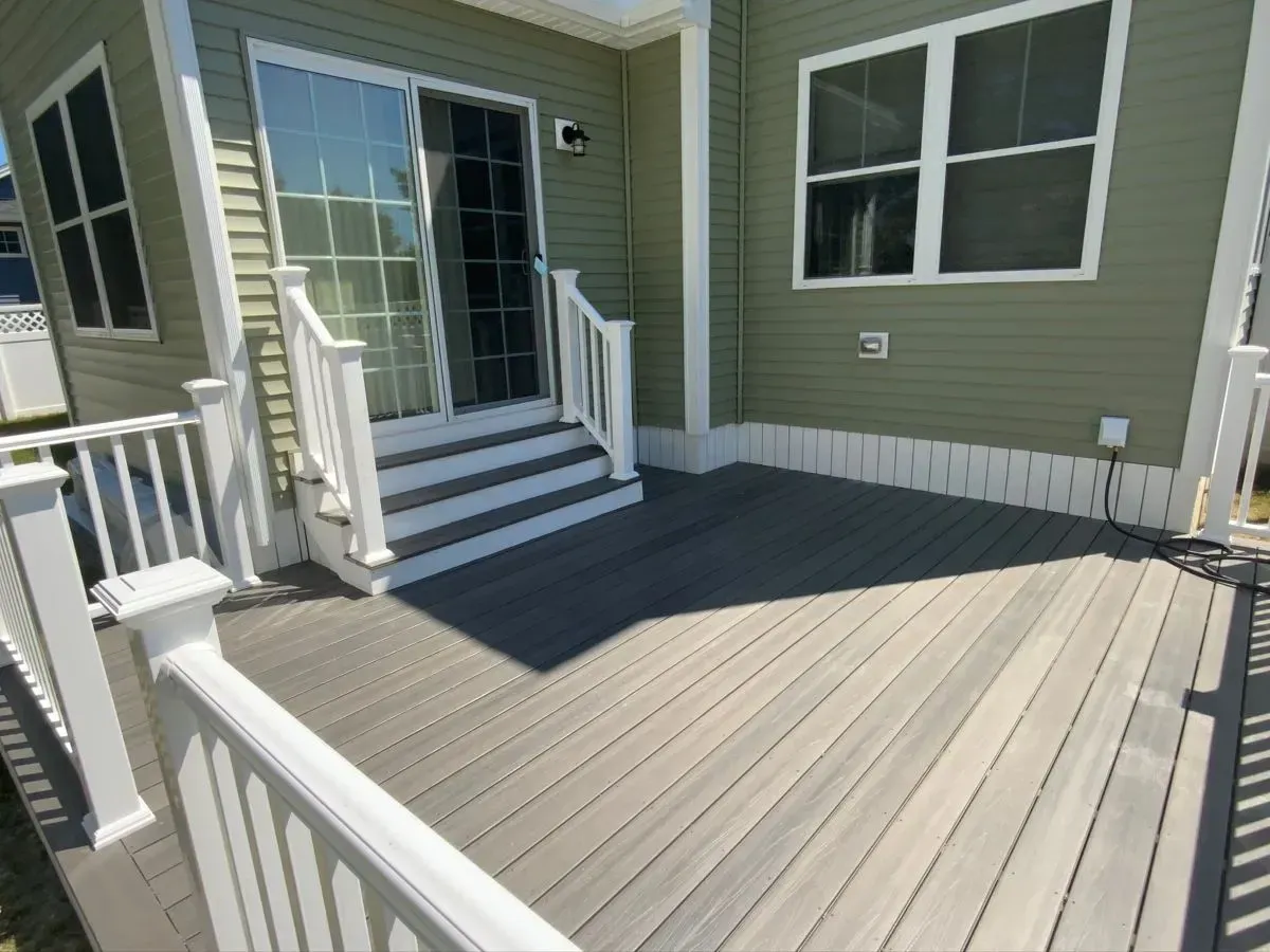 A deck with a white railing and stairs in front of a house.