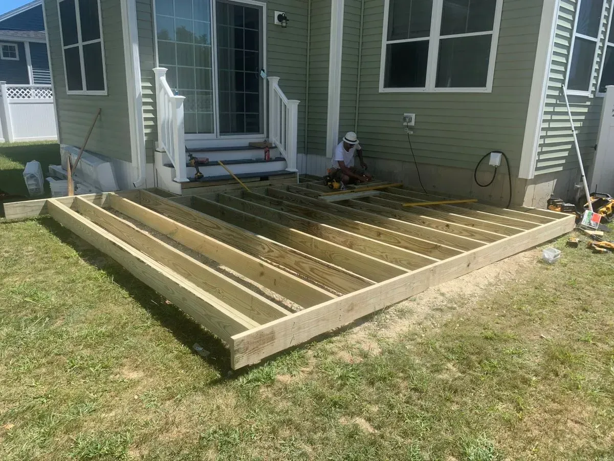 A man is sitting on a wooden deck in front of a house.