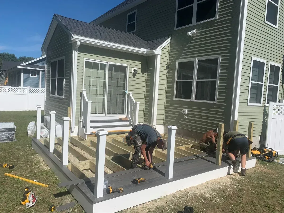 A group of people are working on a deck in front of a house.