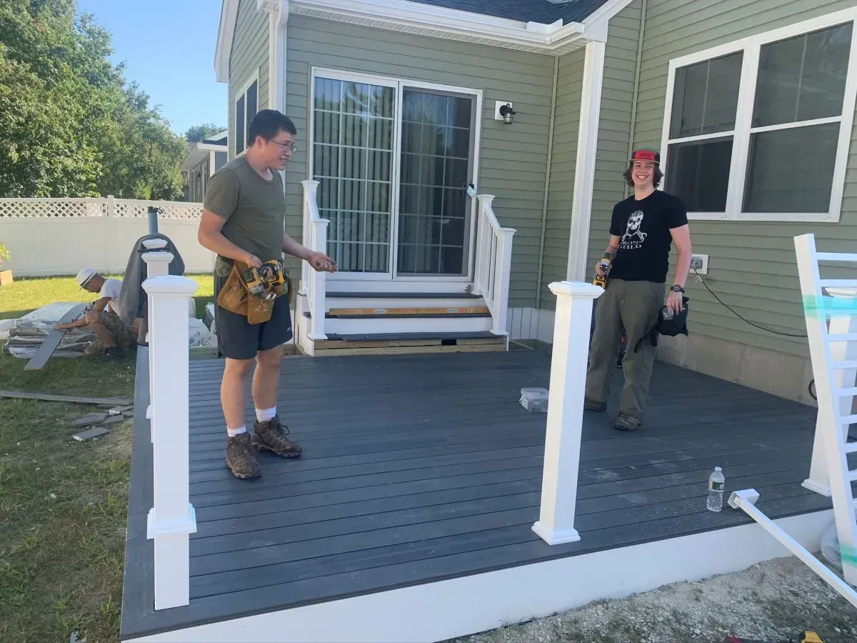 Two men are standing on a deck in front of a house.