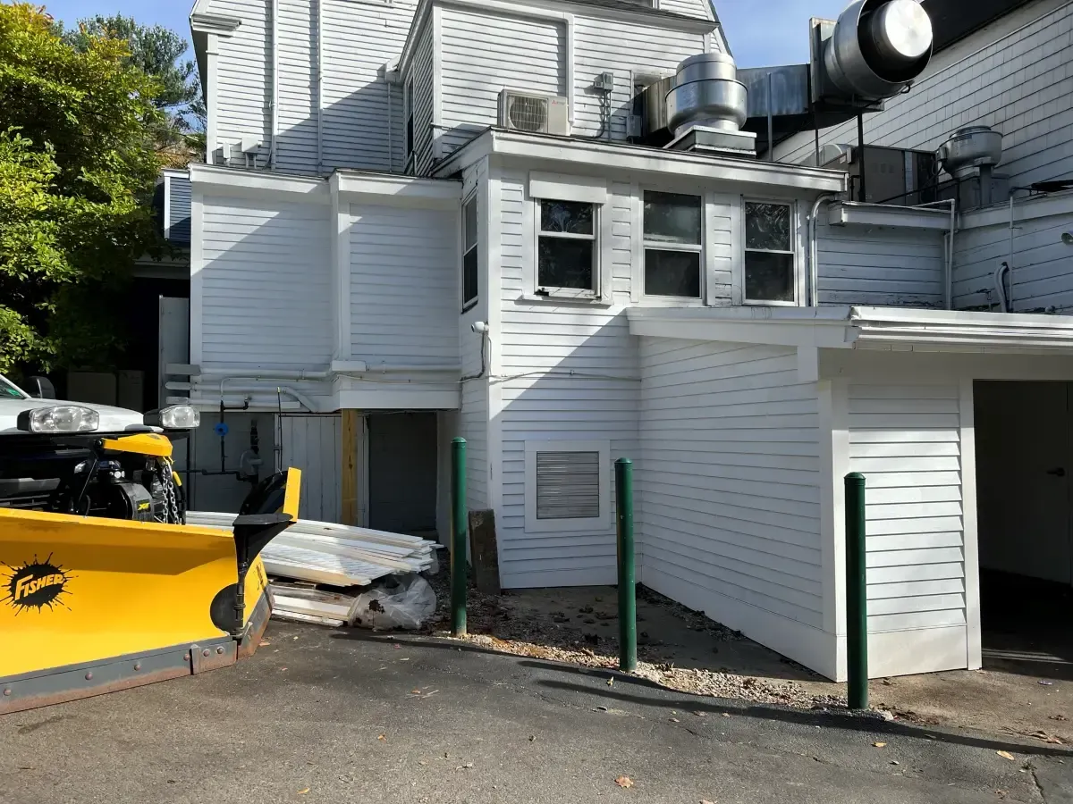 A yellow plow is parked in front of a white building