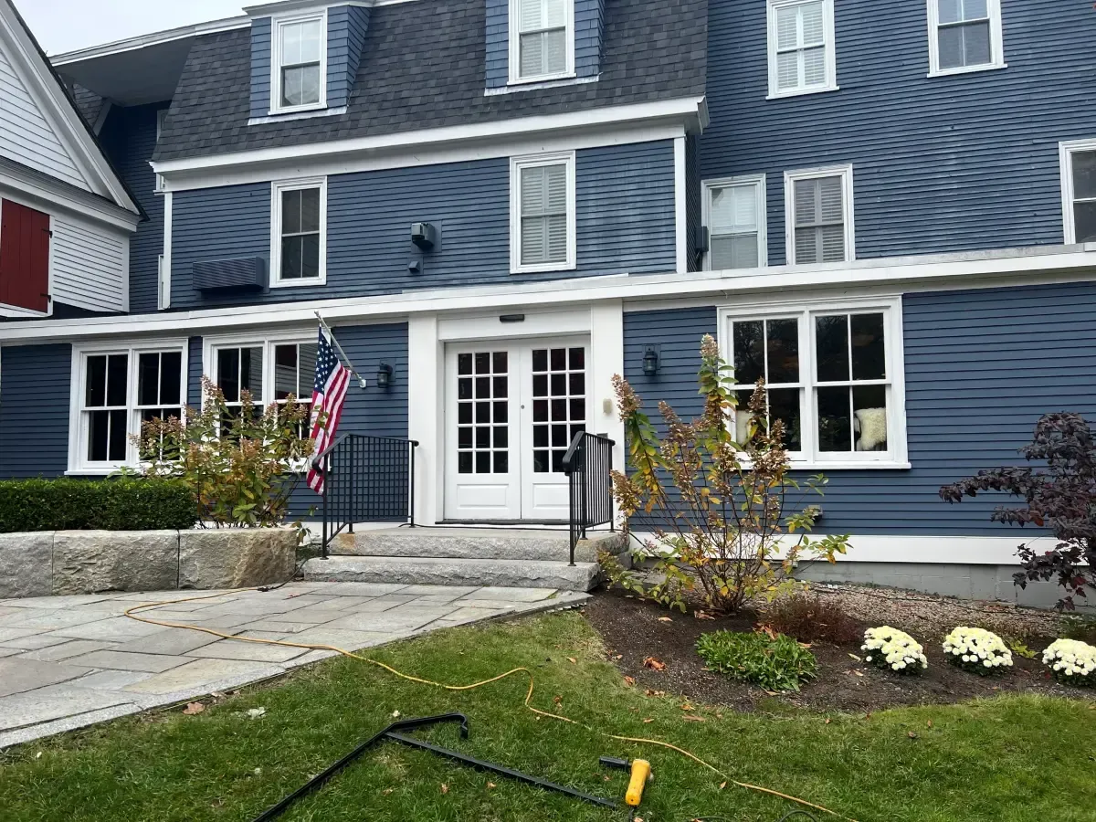 A large blue house with a lot of windows is sitting on top of a lush green lawn.