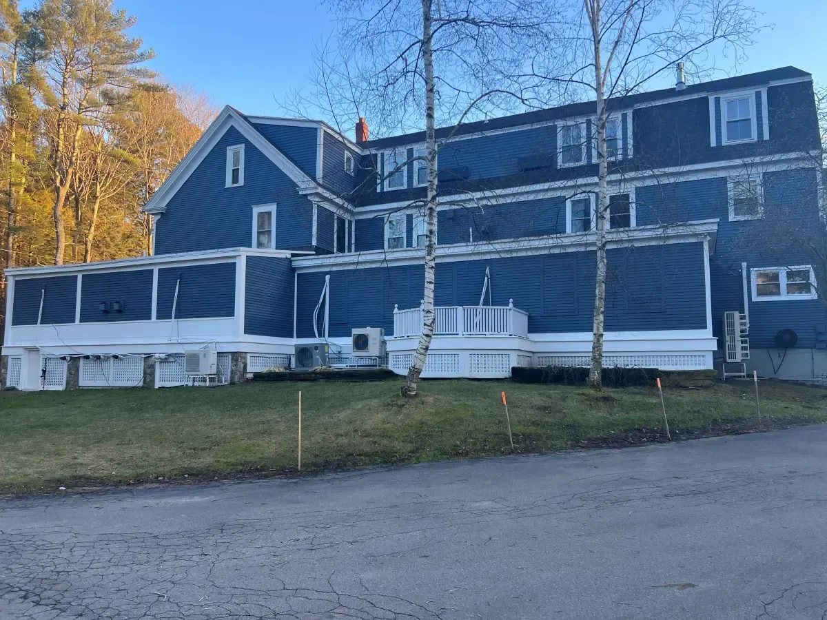 A large blue house with white trim is sitting on top of a lush green field.