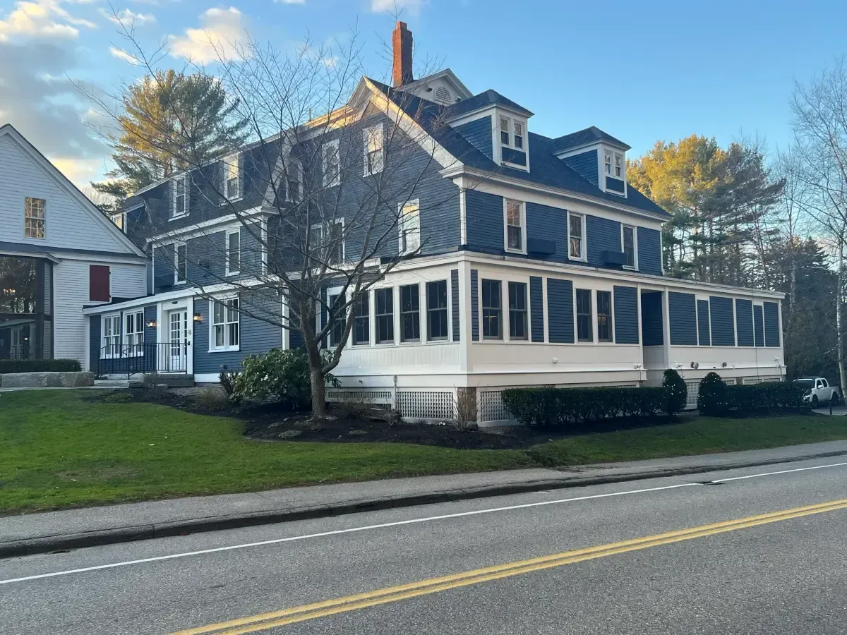 A large house with a large porch is on the side of the road.