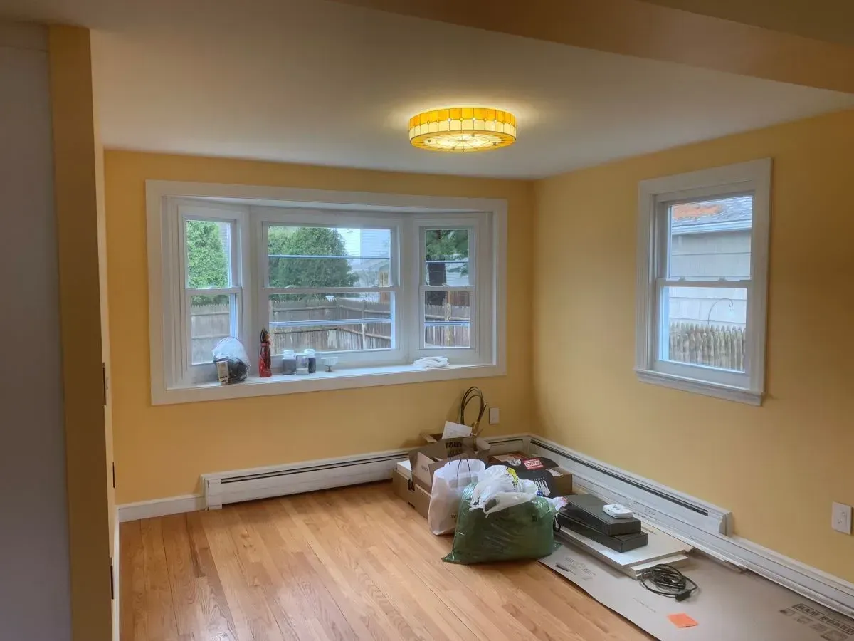 A room with yellow walls and hardwood floors and a large window.