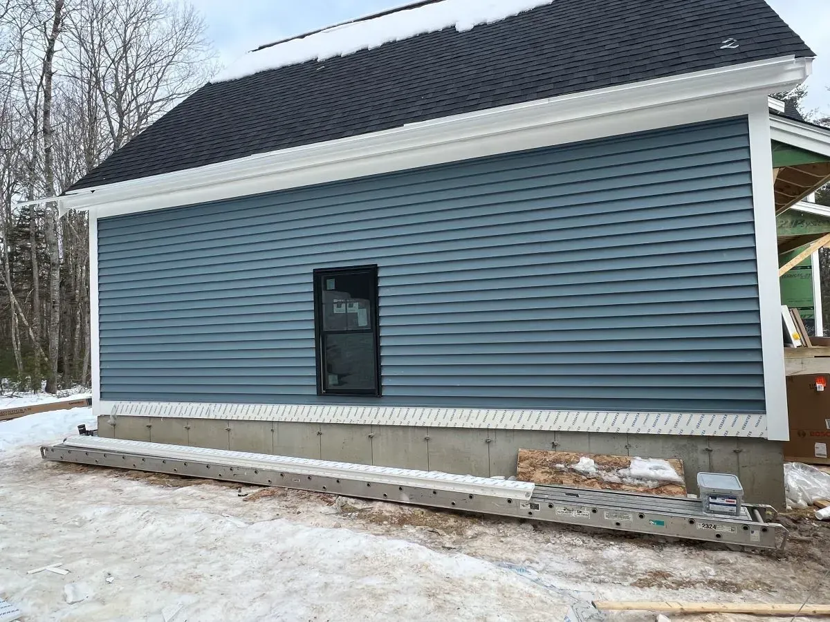 A house with a blue siding and a black roof is being built in the snow.
