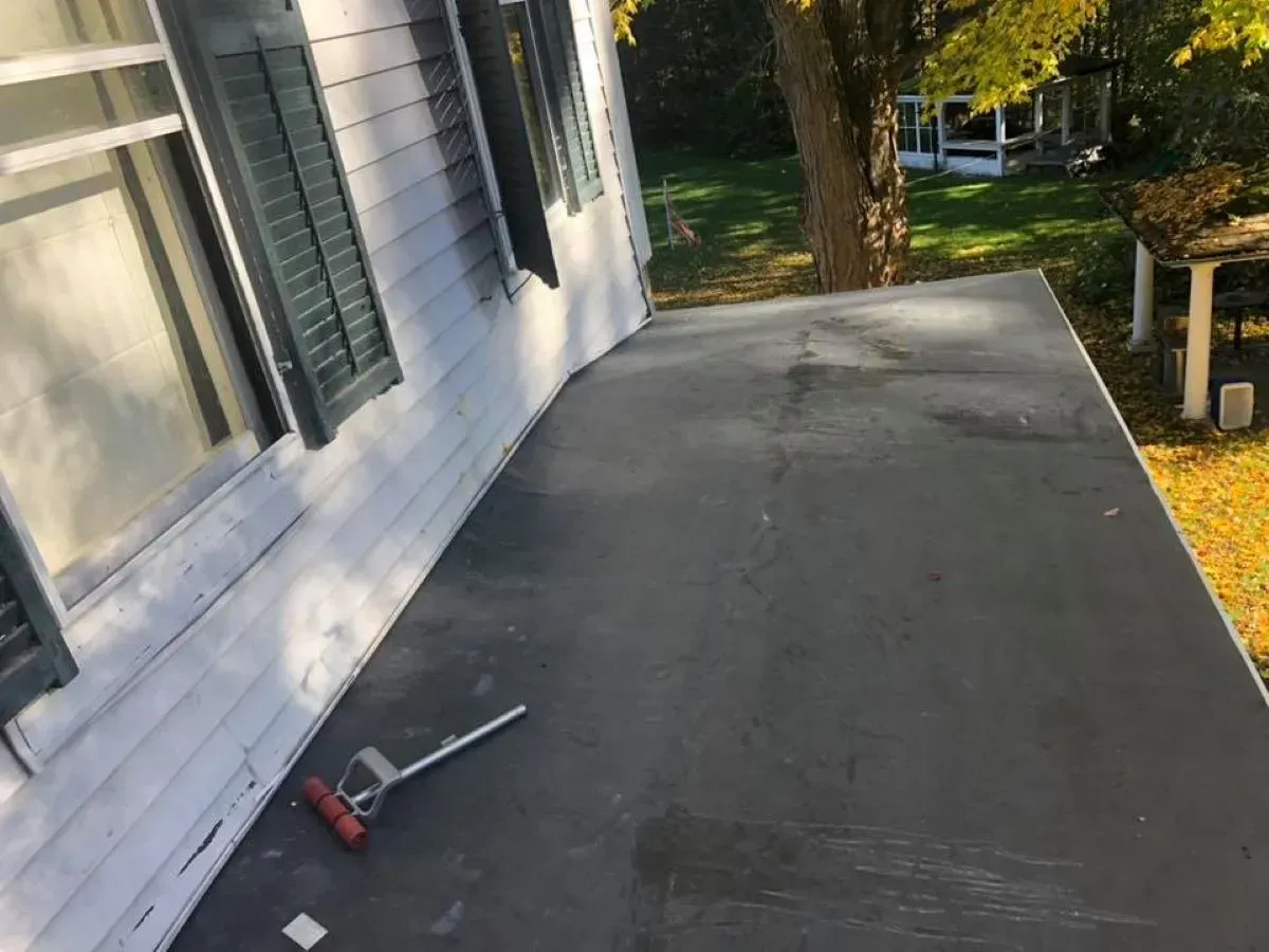 A broom is sitting on a porch next to a house.