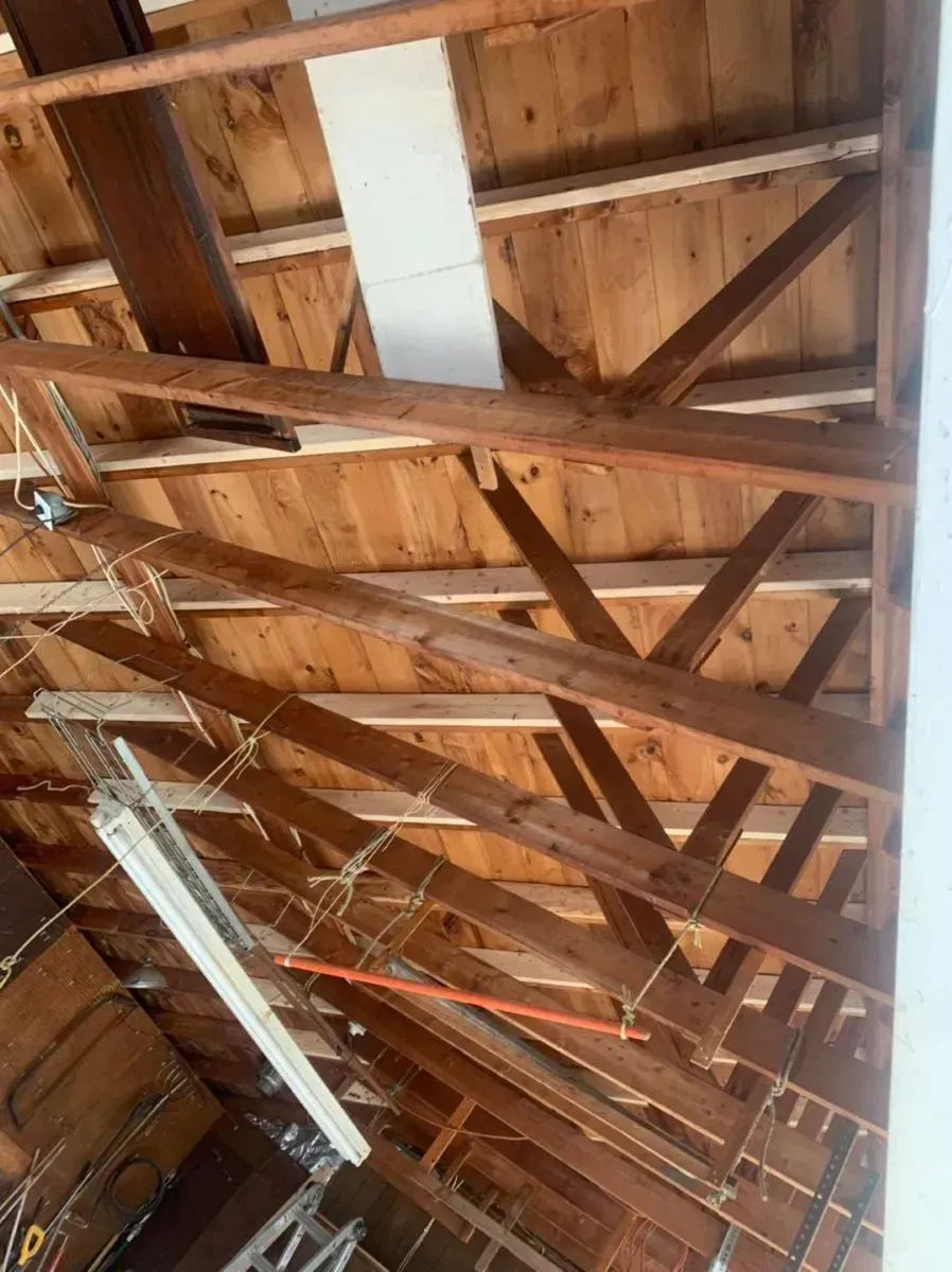 The ceiling of a building with wooden beams and a ladder.
