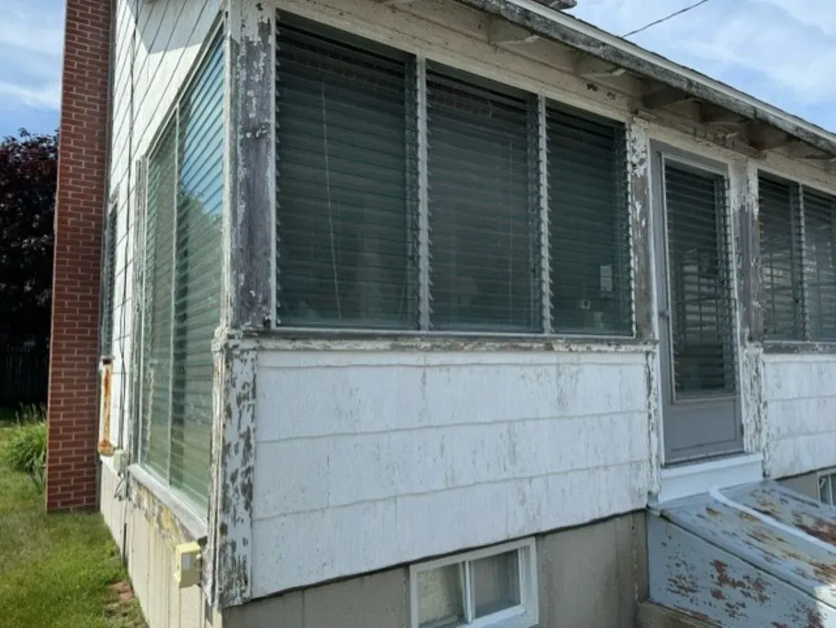 A white house with a screened in porch and a brick chimney.