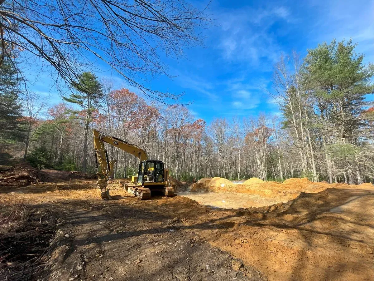 A yellow excavator is digging a hole in the middle of a forest.