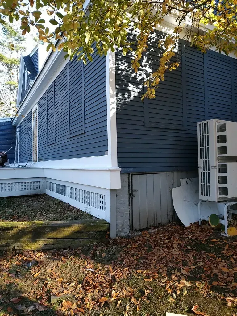The side of a house with a lot of leaves on the ground.