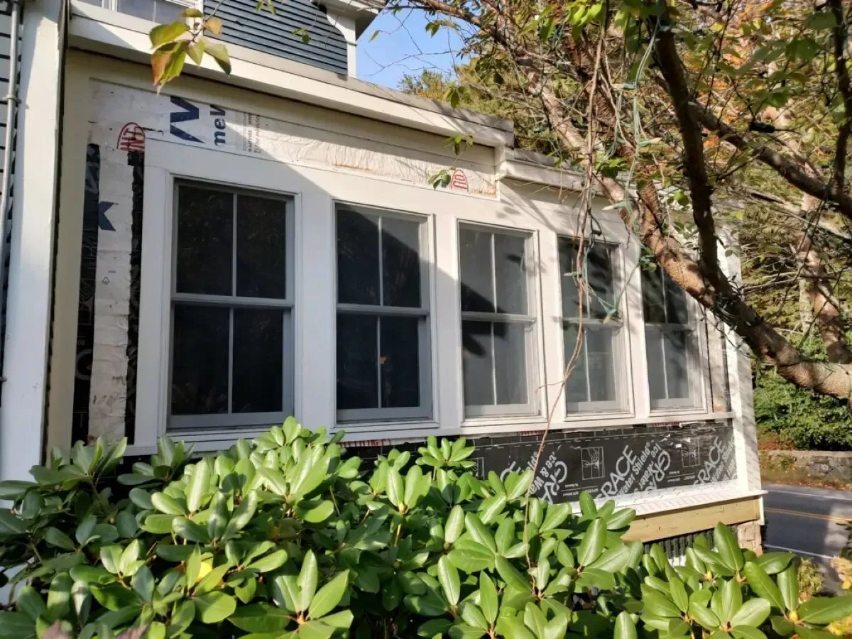 A white house with a porch and a tree in front of it.