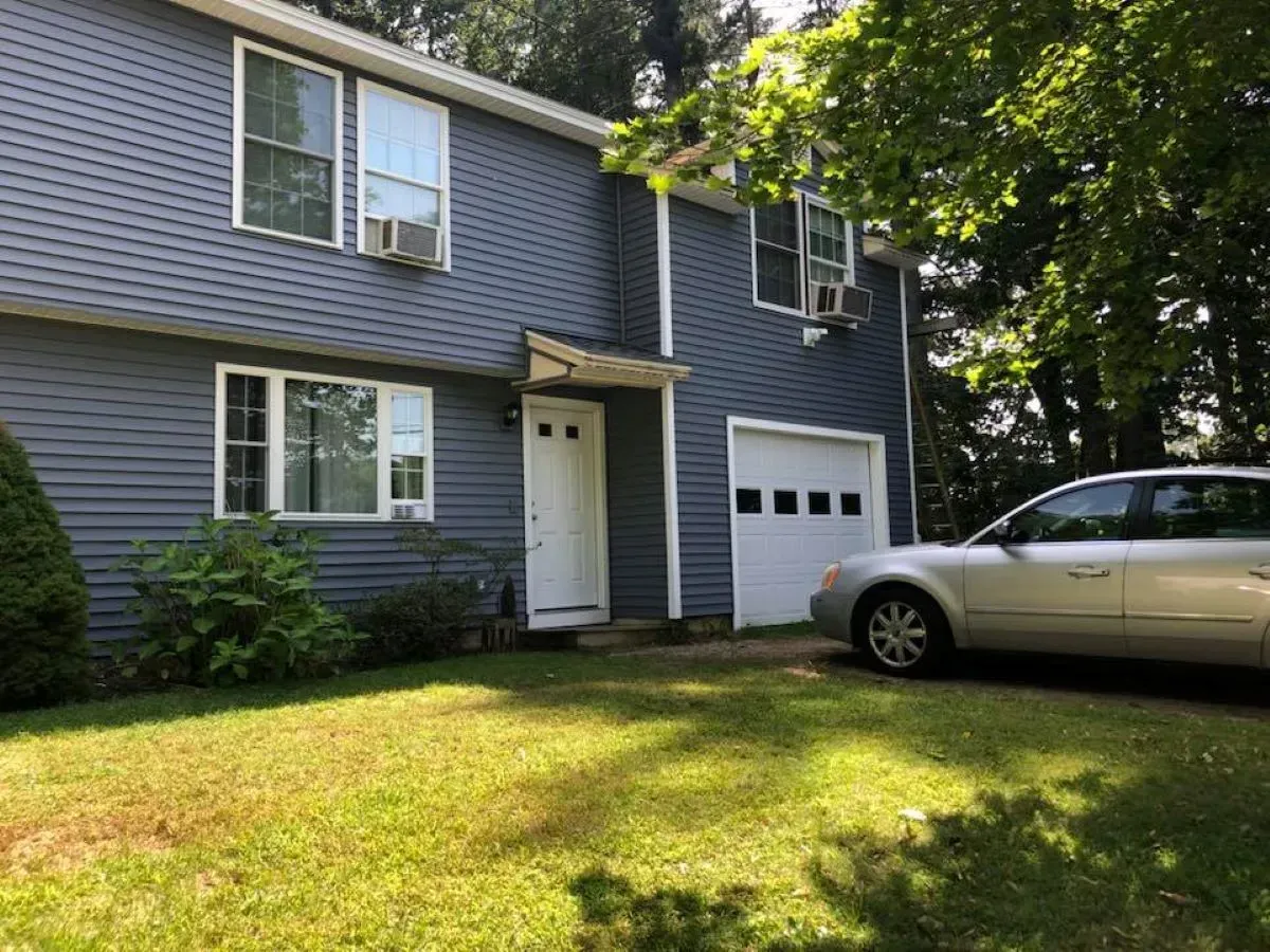 A car is parked in front of a blue house.