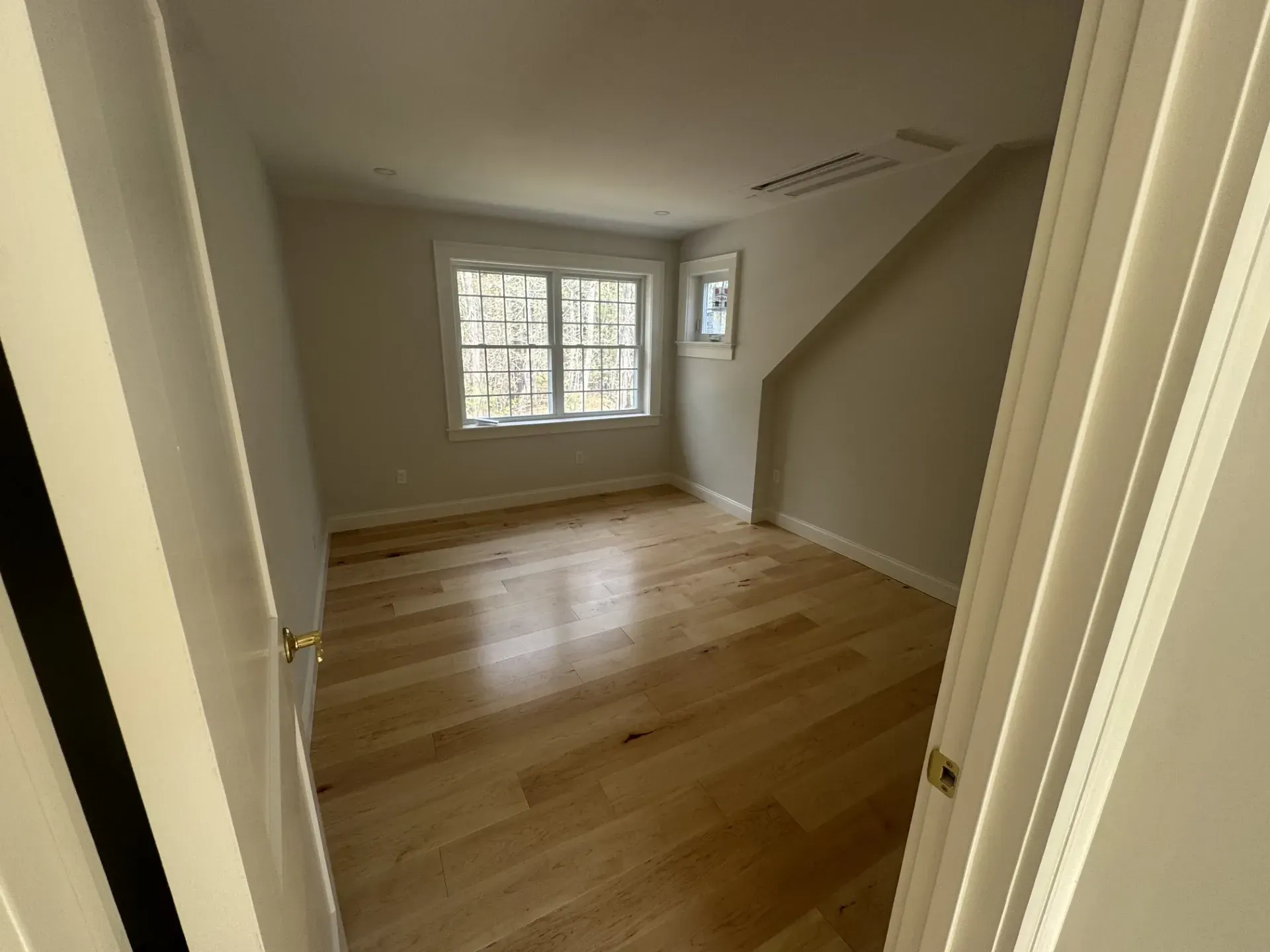 An empty room with hardwood floors and two windows
