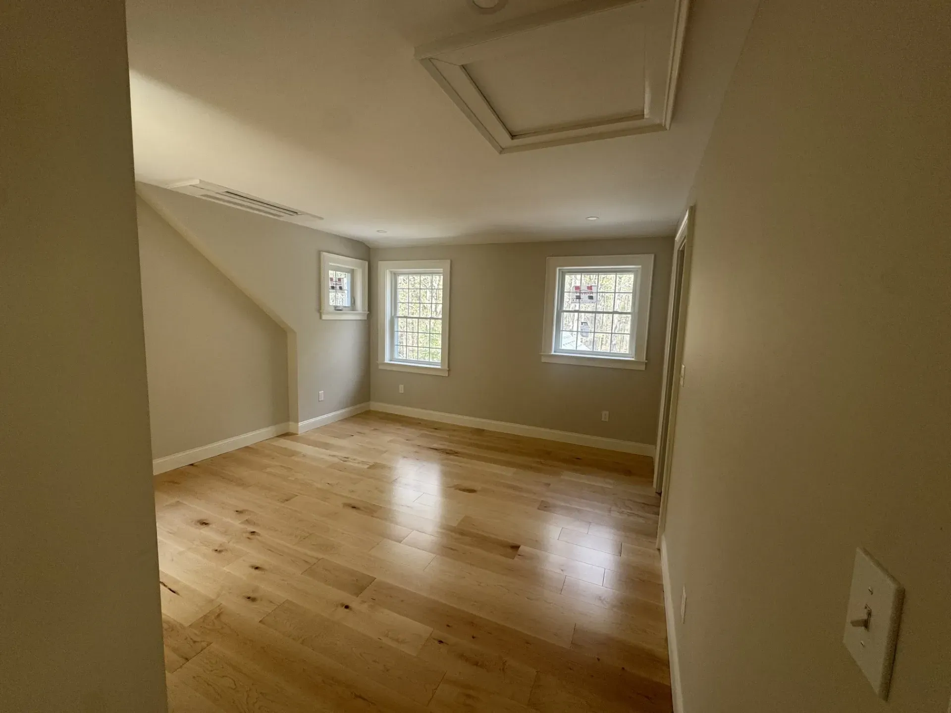 An empty room with hardwood floors and two windows.
