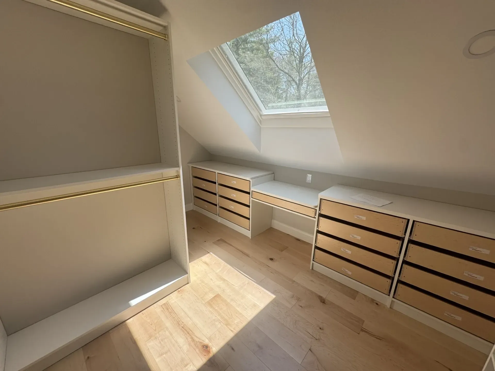A walk in closet with lots of drawers and a skylight.