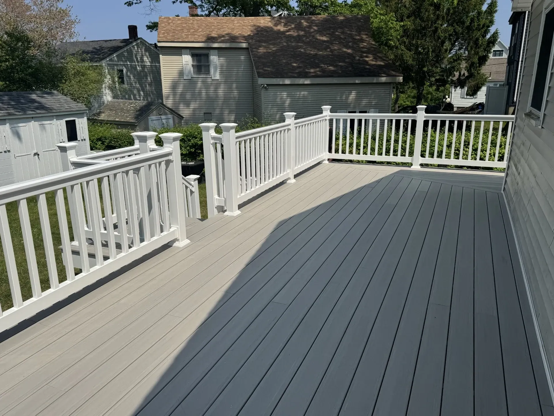 A gray deck with a white railing and a house in the background