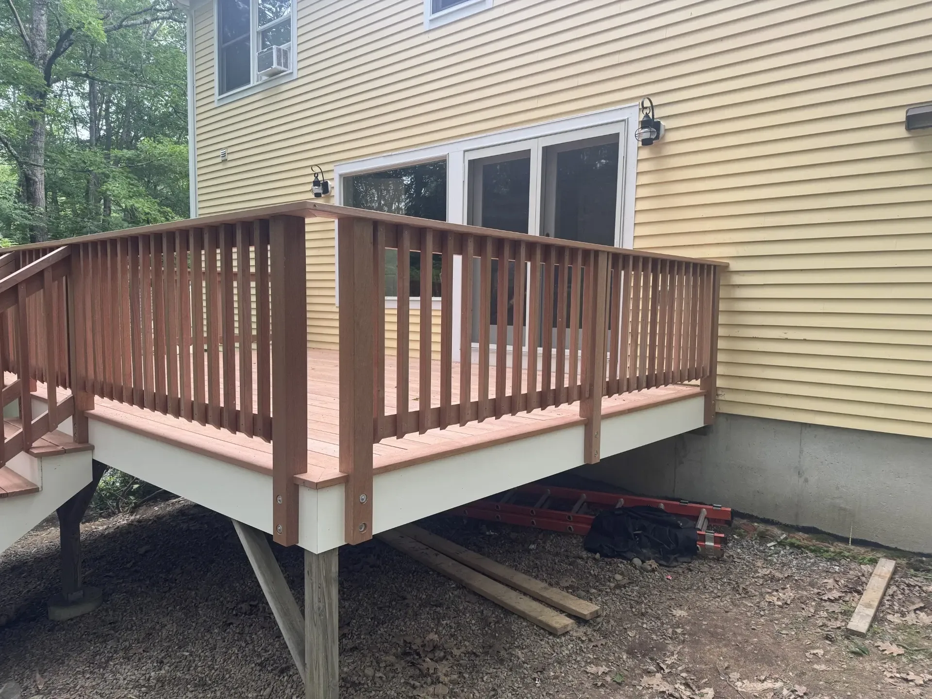 A wooden deck with stairs is sitting in front of a yellow house.