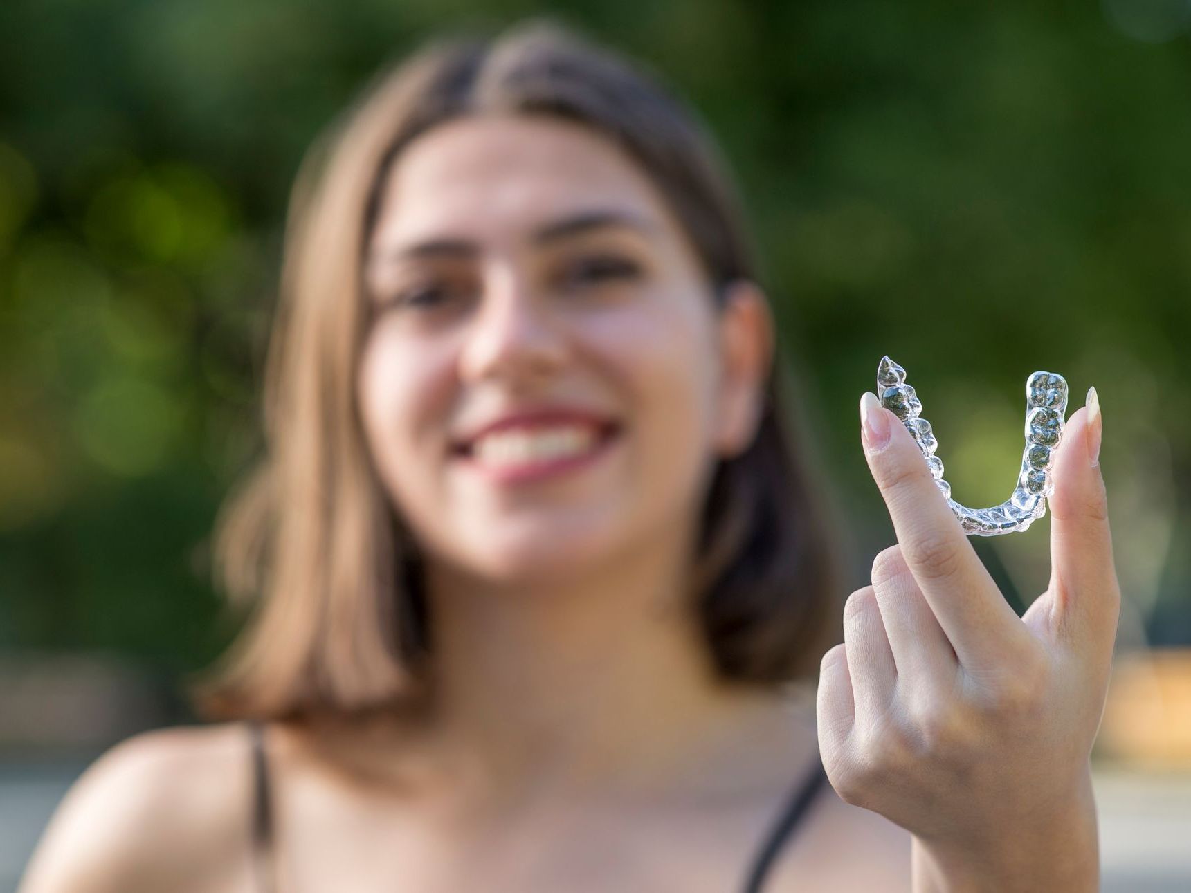 A woman is holding a clear retainer in her hand.