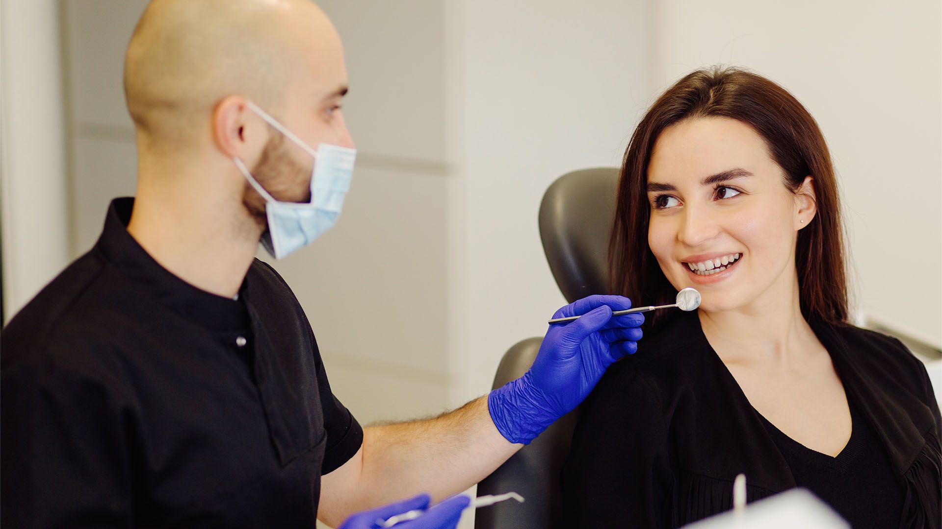 Dentist examining patient's teeth in a dental clinic. Both are smiling.
