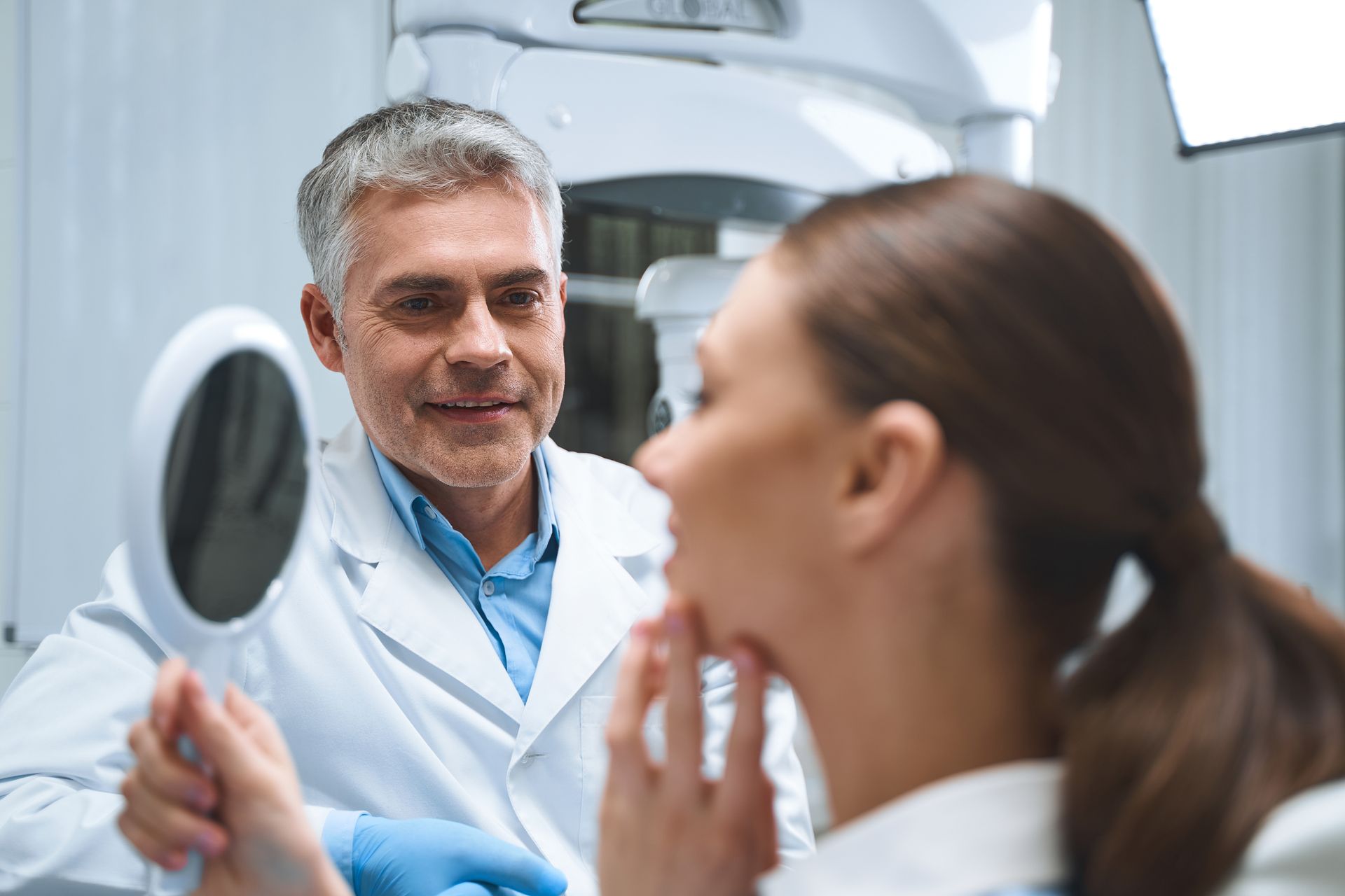 Dentist showing patient her reflection in a mirror; they are in a clinic.