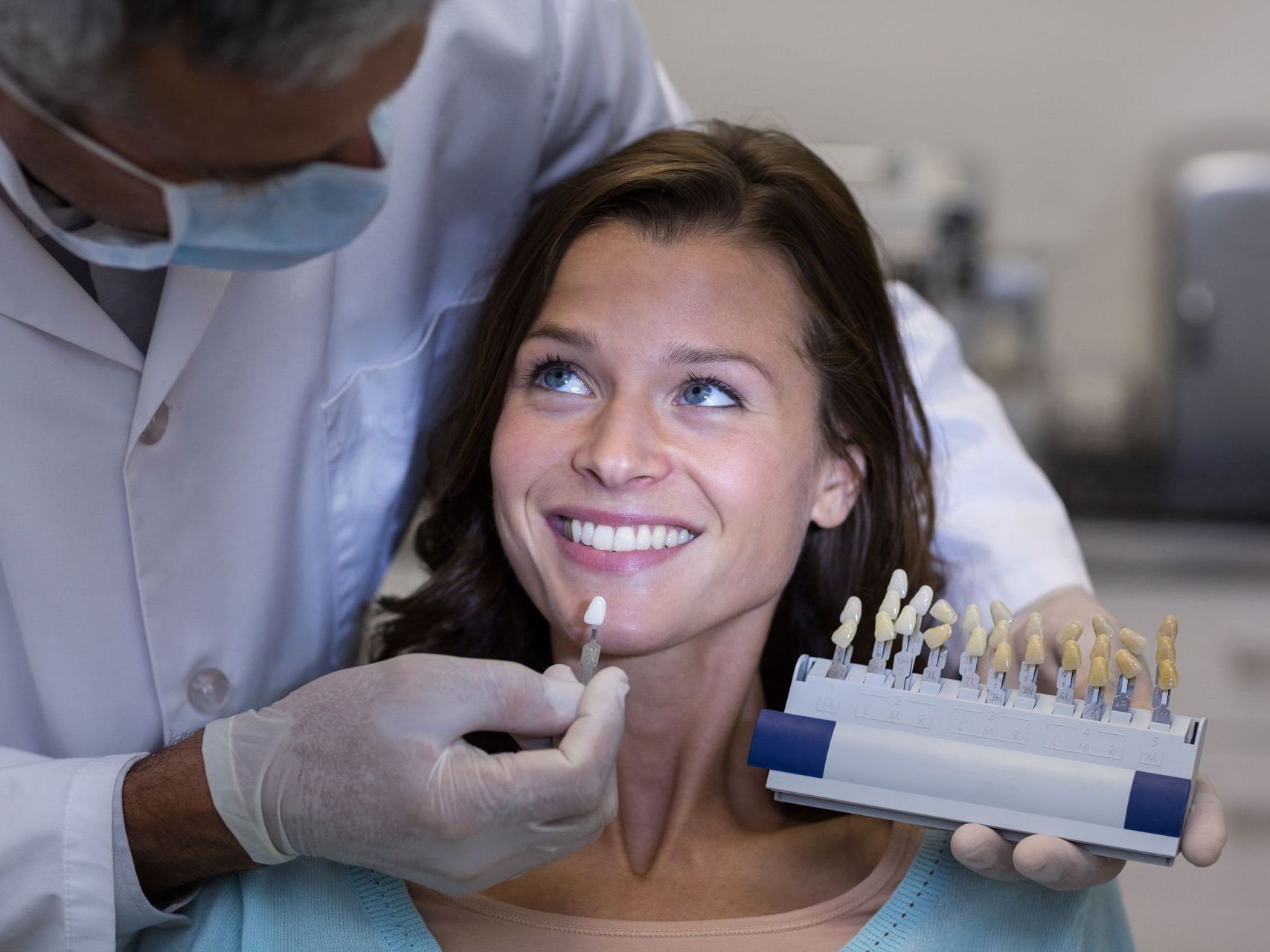 A woman is sitting in a dental chair while a dentist examines her teeth.