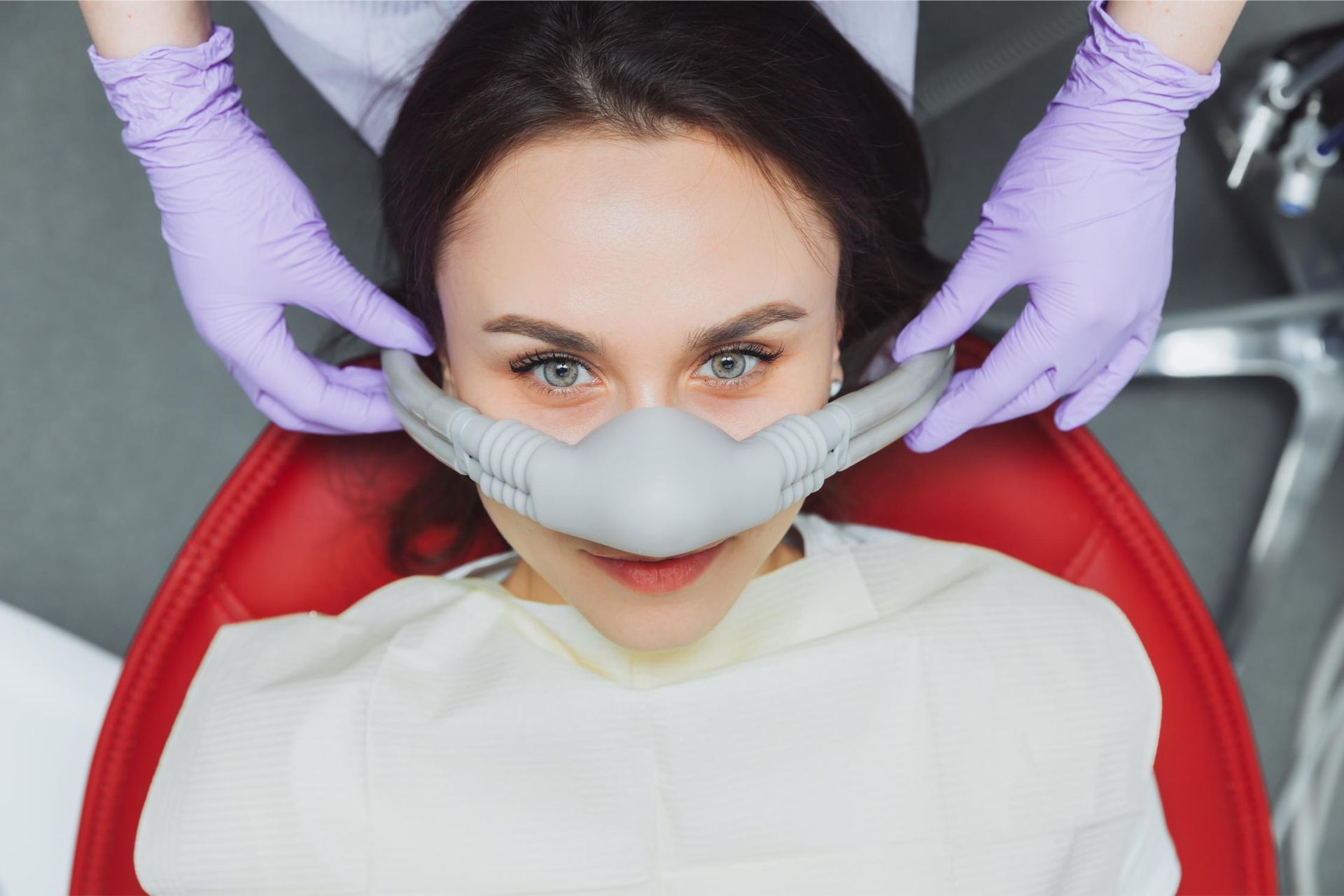 A woman is sitting in a dental chair with an oxygen mask on her face.
