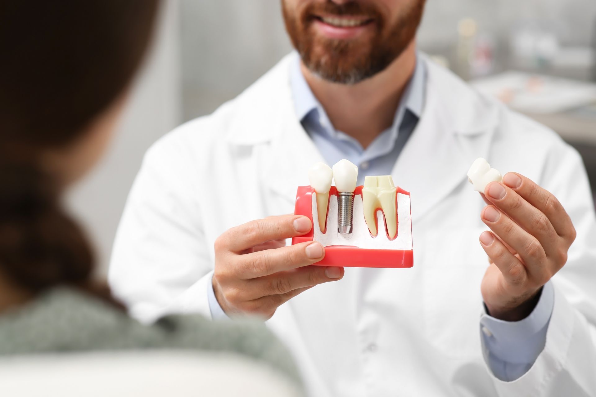 A dentist in a white coat explains a dental implant model to a patient in a clinic.