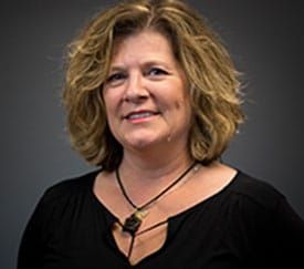 A woman with blonde hair is wearing a black shirt and a necklace.