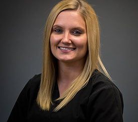 The woman is wearing a black scrub and smiling for the camera.