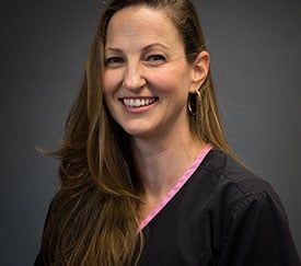 A woman wearing a black scrub top and earrings is smiling for the camera.