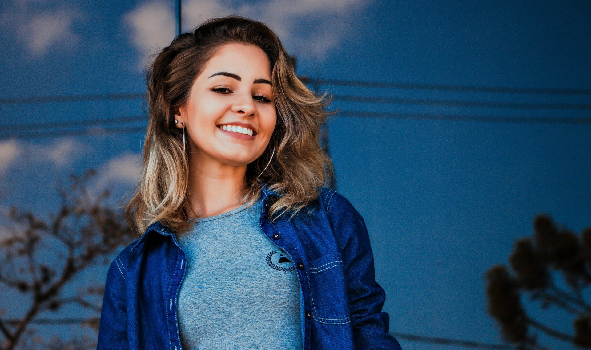 A woman wearing a blue jacket and a gray shirt is smiling.