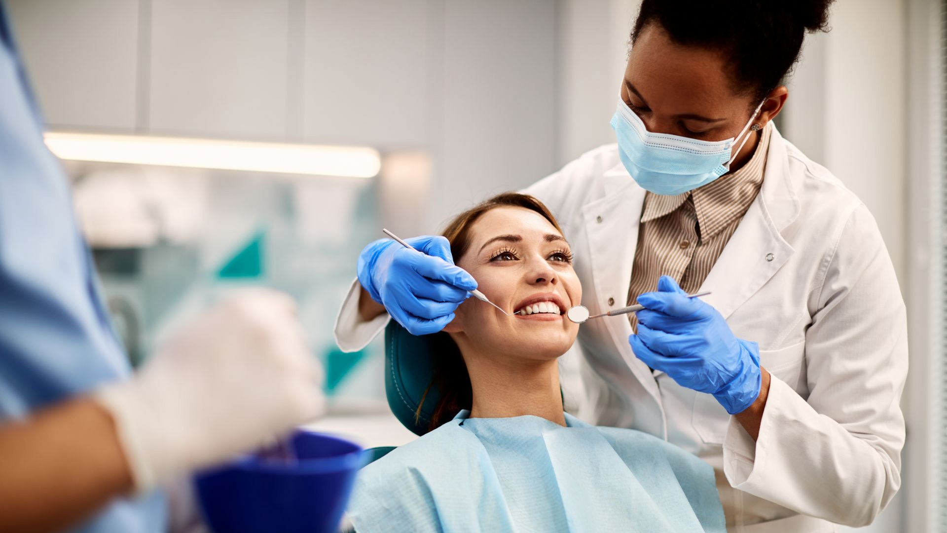 Dentist in mask and gloves examining patient's teeth with dental instruments; in a dentist's office.