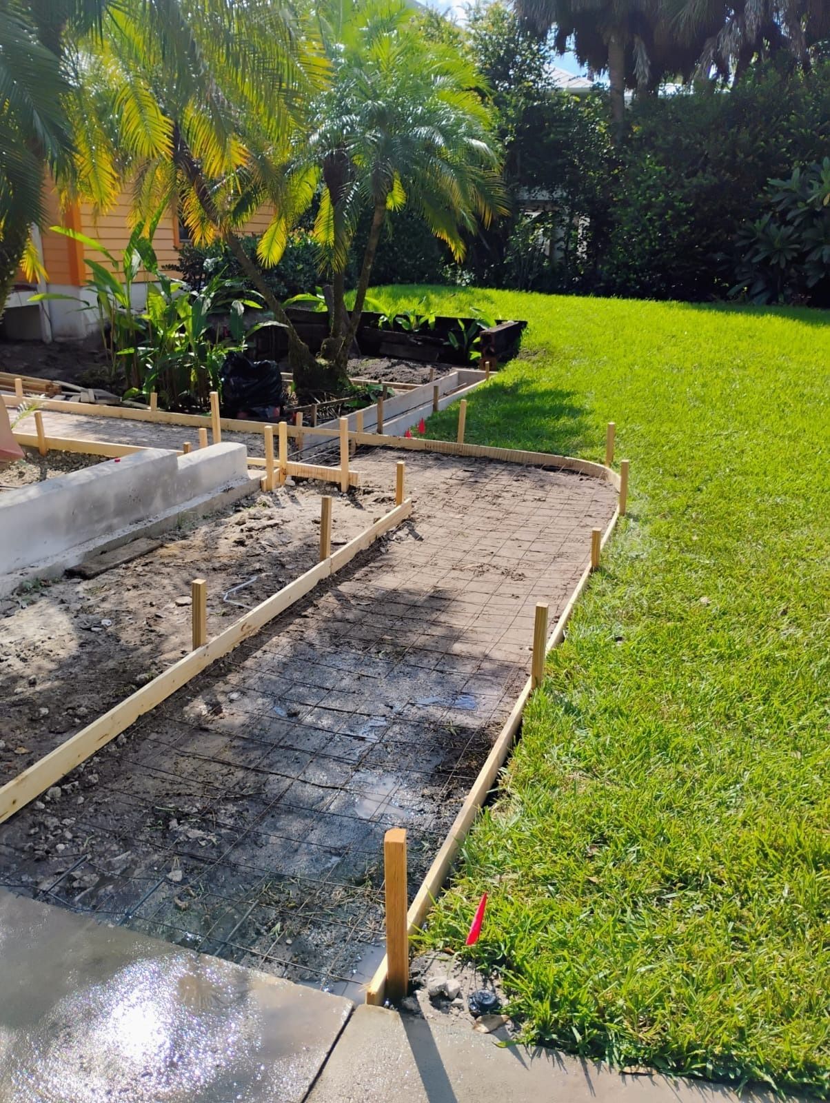 A concrete walkway is being built in the backyard of a house.