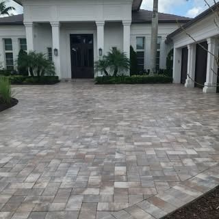 A large white house with a brick driveway in front of it.