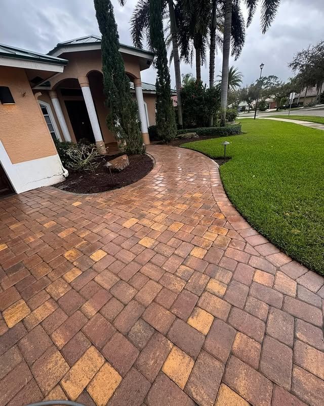 A brick walkway leading to a house with palm trees in the background.