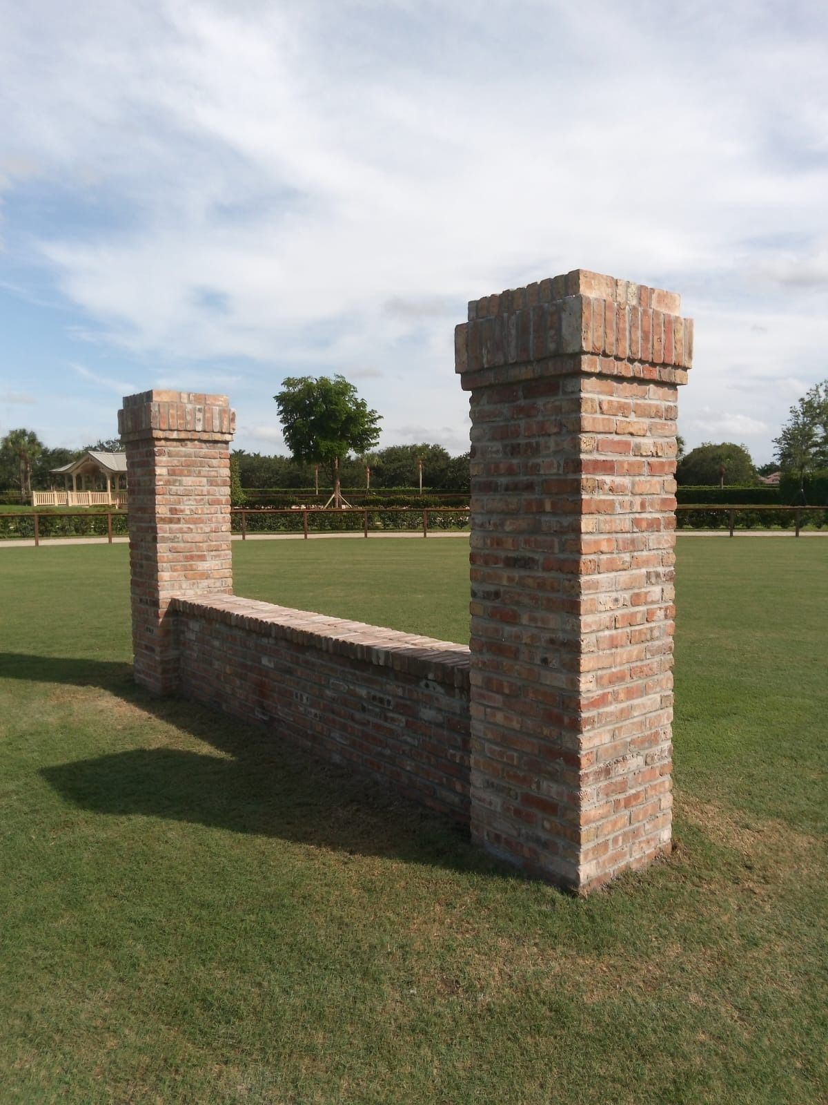 Two brick pillars in a grassy field with trees in the background