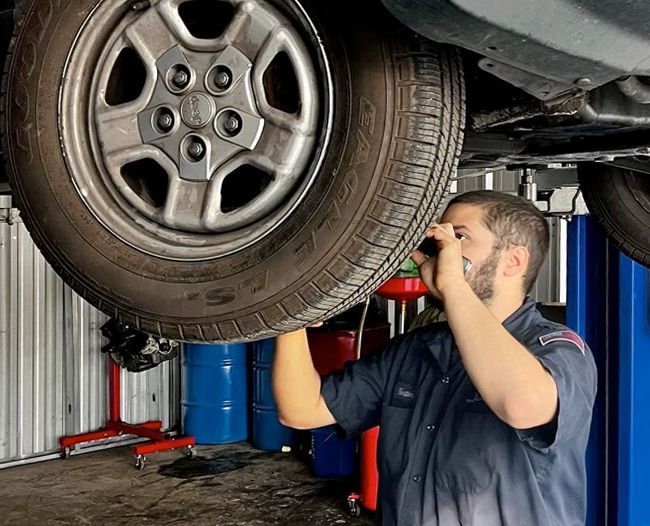 Mechanic inspecting car tire under a lift in a garage.