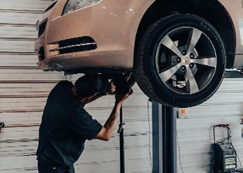Mechanic working on a car lifted on a hydraulic hoist in a garage.