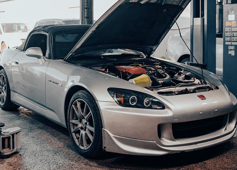 Silver Honda S2000 with hood open in a garage.