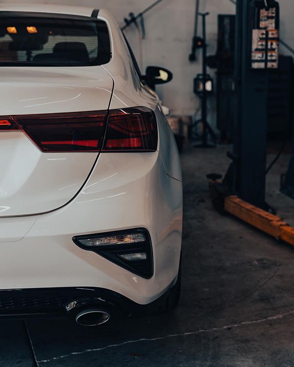White car's rear end inside a garage. Red taillight and black exhaust.