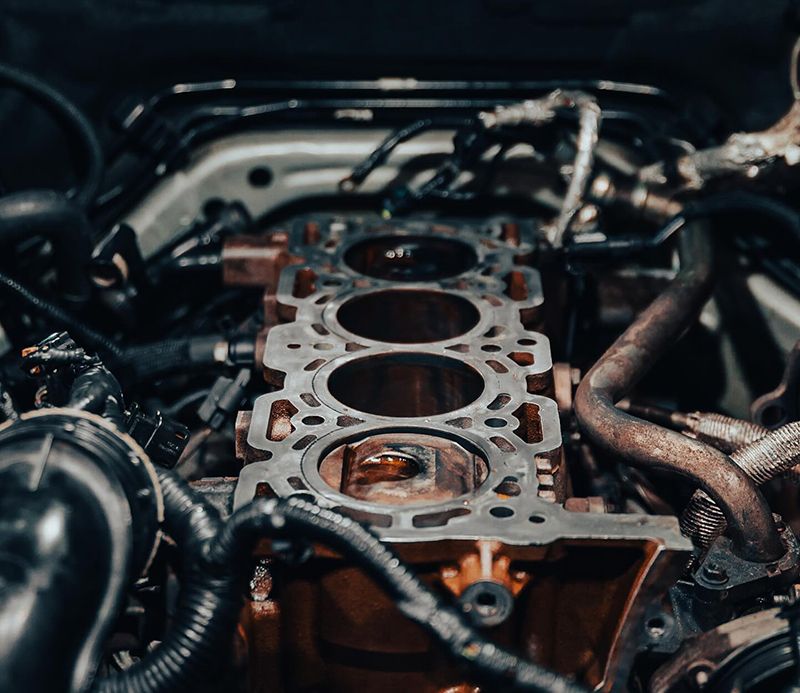 Engine block with cylinders exposed, surrounded by hoses and wires, in a garage setting.