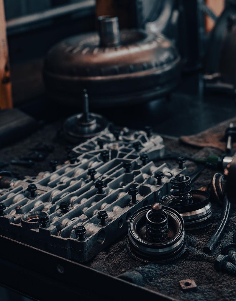 Car transmission parts on a workbench, featuring a valve body, torque converter, and other components.