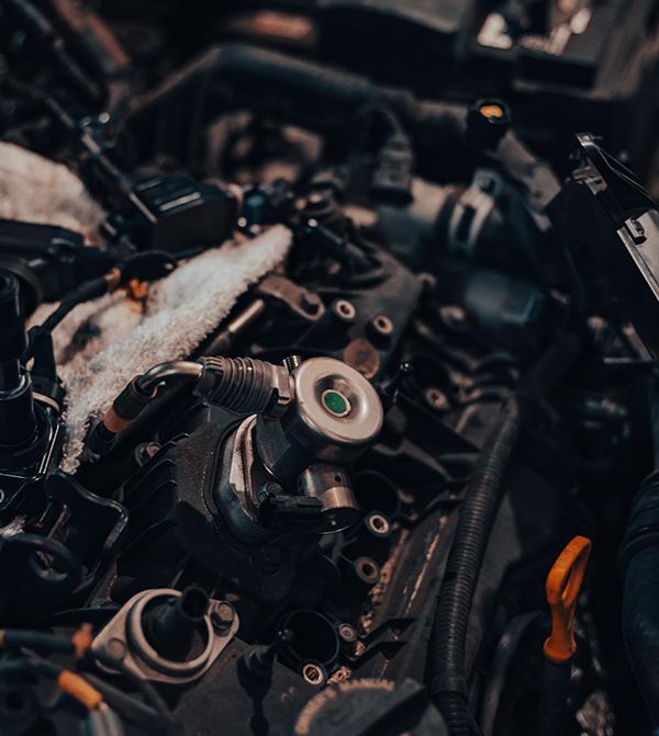 Car engine close-up view with various components, focus on fuel injector, tools visible, dark setting.