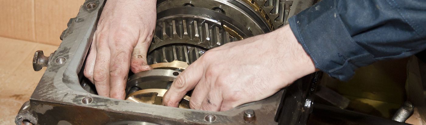 Hands working inside the housing of a greasy mechanical transmission assembly.