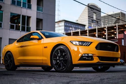 Yellow Ford Mustang sports car with black rims parked on city street.